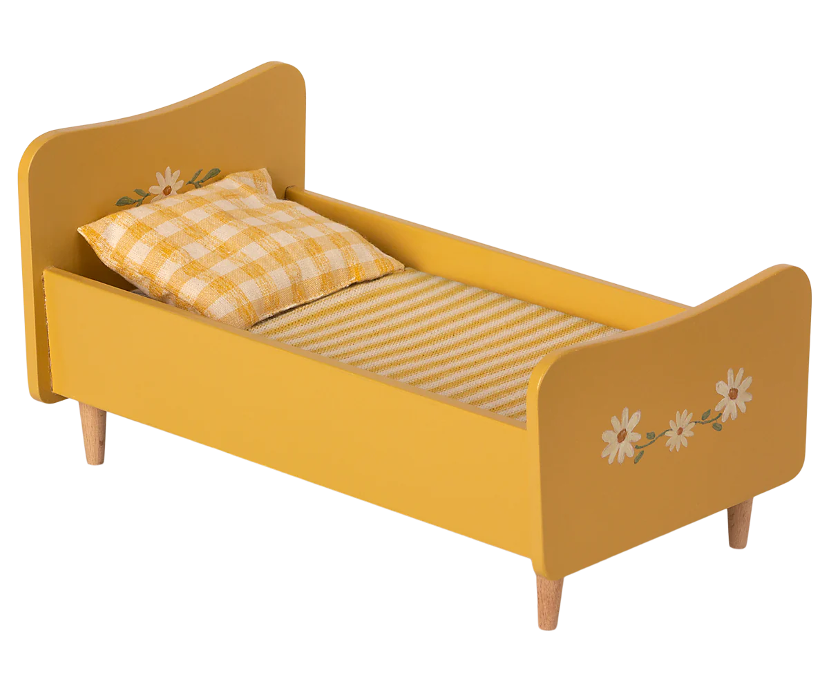 The Maileg Wooden Bed, Mini is a charming toddler bed in yellow, featuring hand-painted floral decorations on both the headboard and footboard. This delightful piece comes with a checked pillow and a striped blanket and is supported by four sturdy wooden legs, making it an enchanting choice for any child's room.